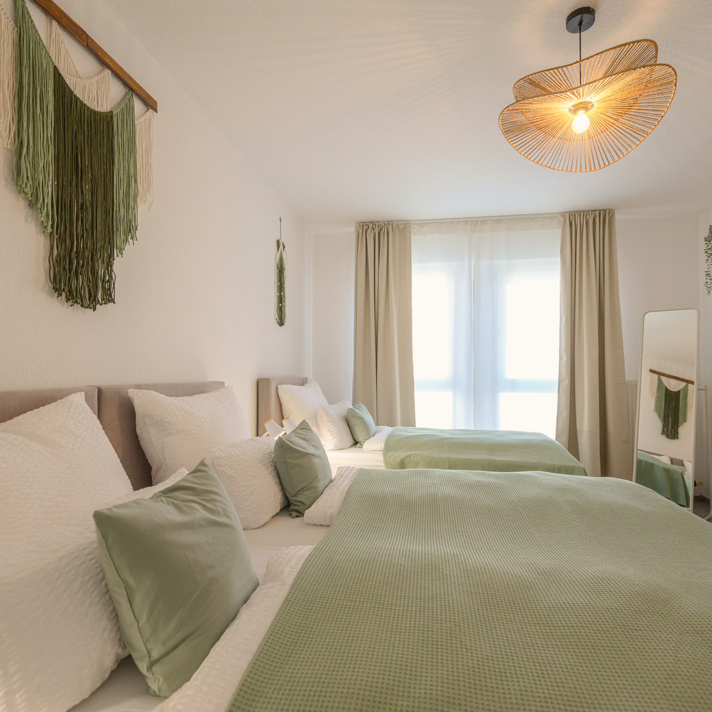 Schlafzimmer der Wohnung Maxi I mit Doppelbett unter der Dachschräge, Holz-Nachttischen und großer Bambus-Hängeleuchte